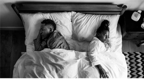 Couple in bed turned away from each other, showing emotional distance